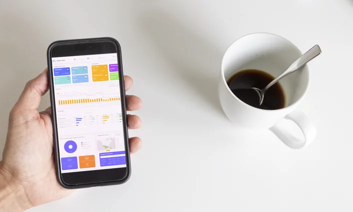 Werbeanzeigen auf Social Media Hand hält ein Smartphone mit einem Werbeanzeigen-Dashboard neben einer Kaffeetasse