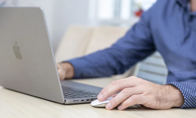 Hand an der Maus neben einem Laptop am Schreibtisch