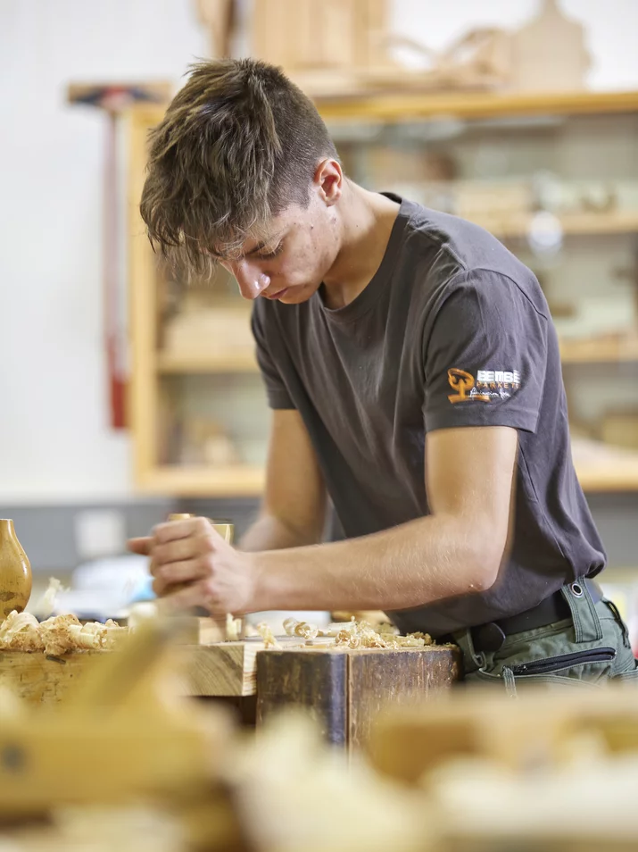 Foto einer Person bei der Holzverarbeitung Junger Schreiner bearbeitet ein Werkstück in einer Holzwerkstatt